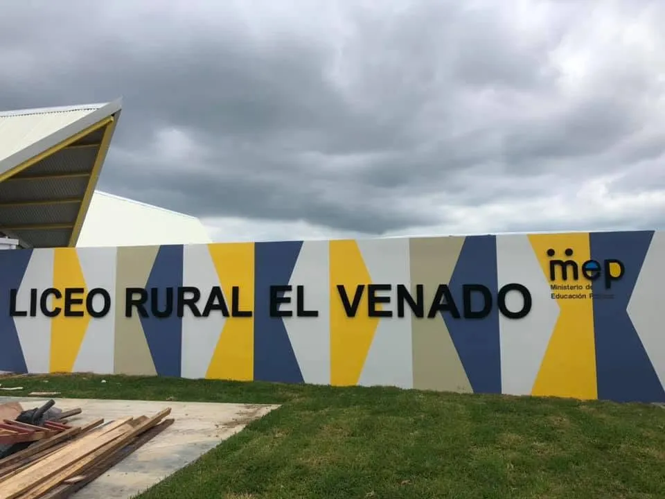 Muro de acceso del Liceo Rural El Venado con el logotipo del MEP y el edificio del colegio al fondo